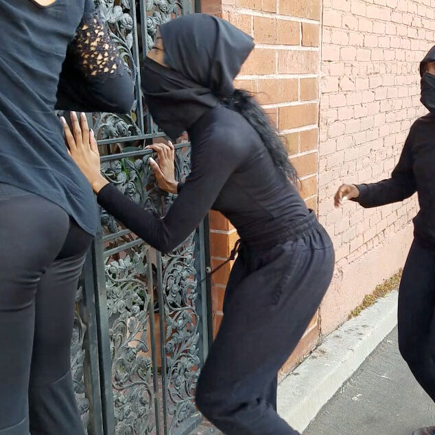 Young girls in black suits and mask running a closed fence