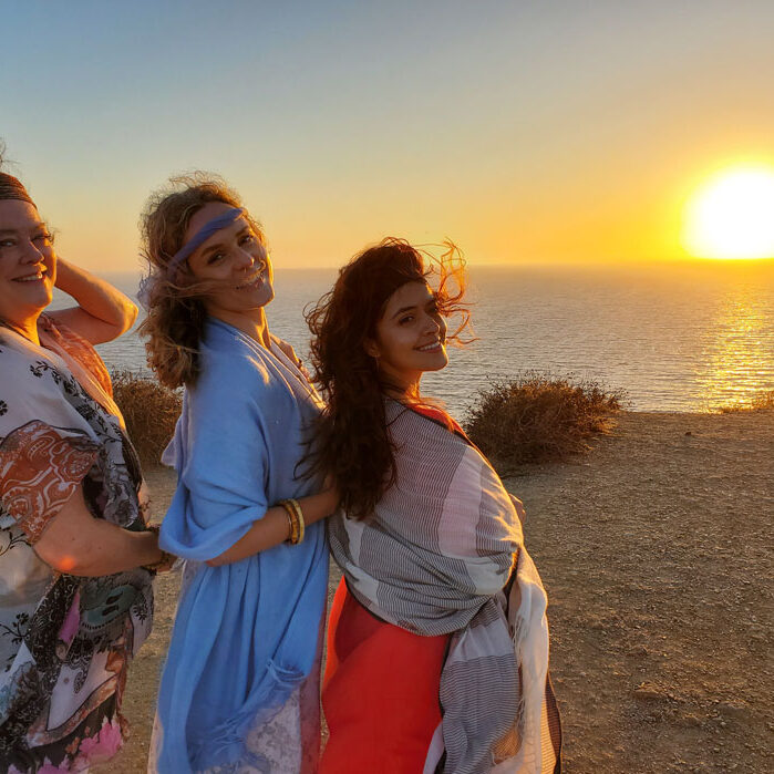 Three woman looking over their shoulders to the camera with the sunset behind them