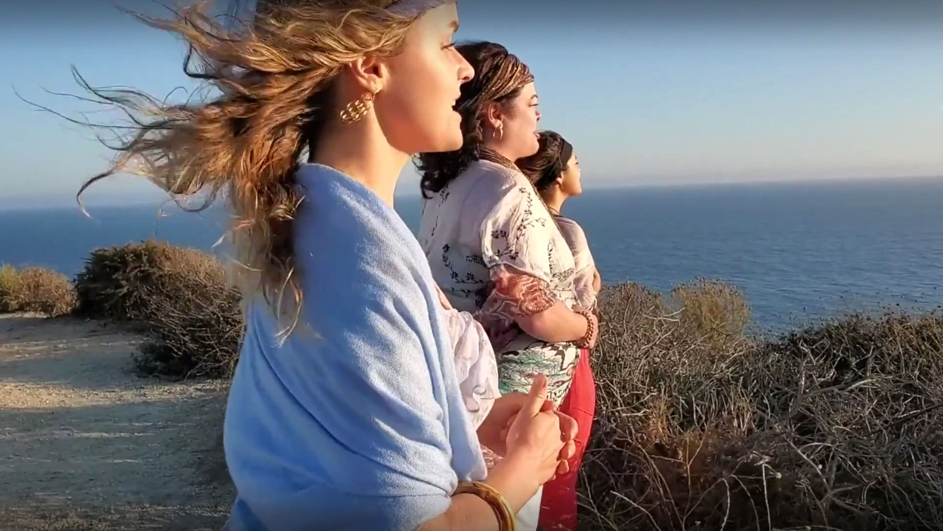 Three woman standing on a beach edge looking out to the ocean