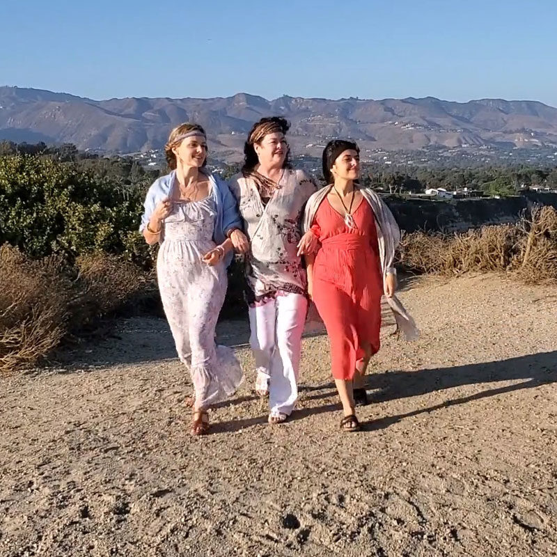 Three girls walking arm and arm along a beachy cliff